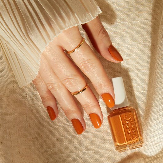 Sigourney smiling and holding a bottle of essie nail polish in the shade unguilty pleasures